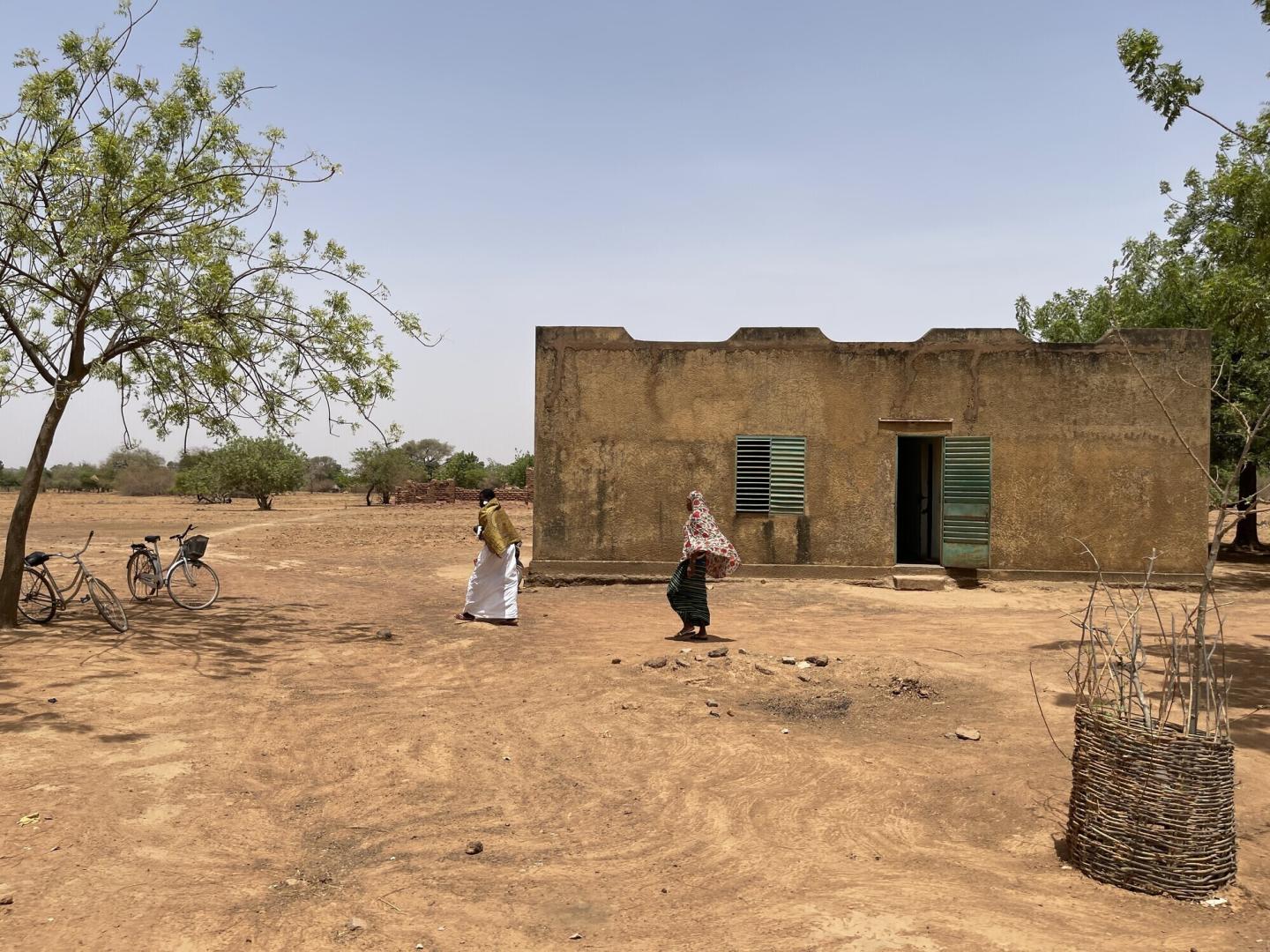 Two people walk past a building in rural Burkina Faso