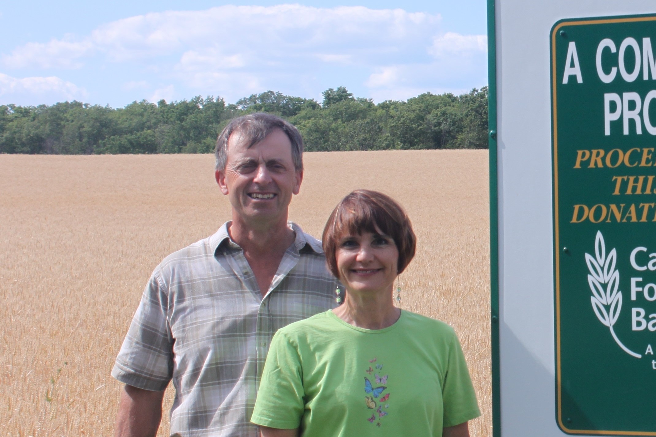 Two people standing in a field next to a sign for Canadian Foodgrains Bank
