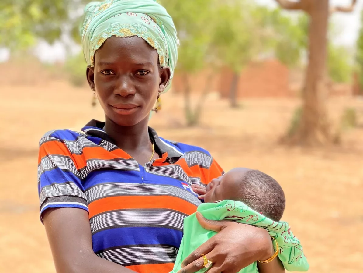 A woman holds her baby and looks at the camera