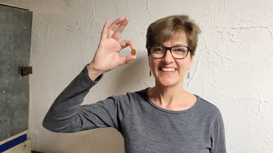A smiling woman with glasses holds up a copper penny
