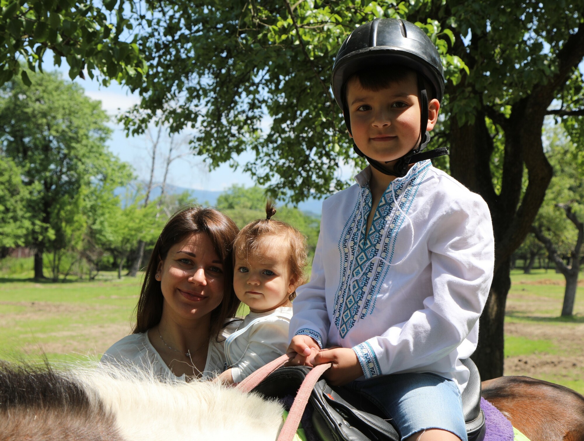 A woman holding a small child standing next to a boy riding a horse