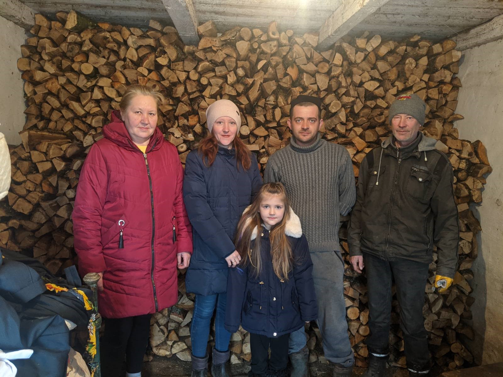 A displaced family from Ukraine stands in front of firewood given to them by donors. 
