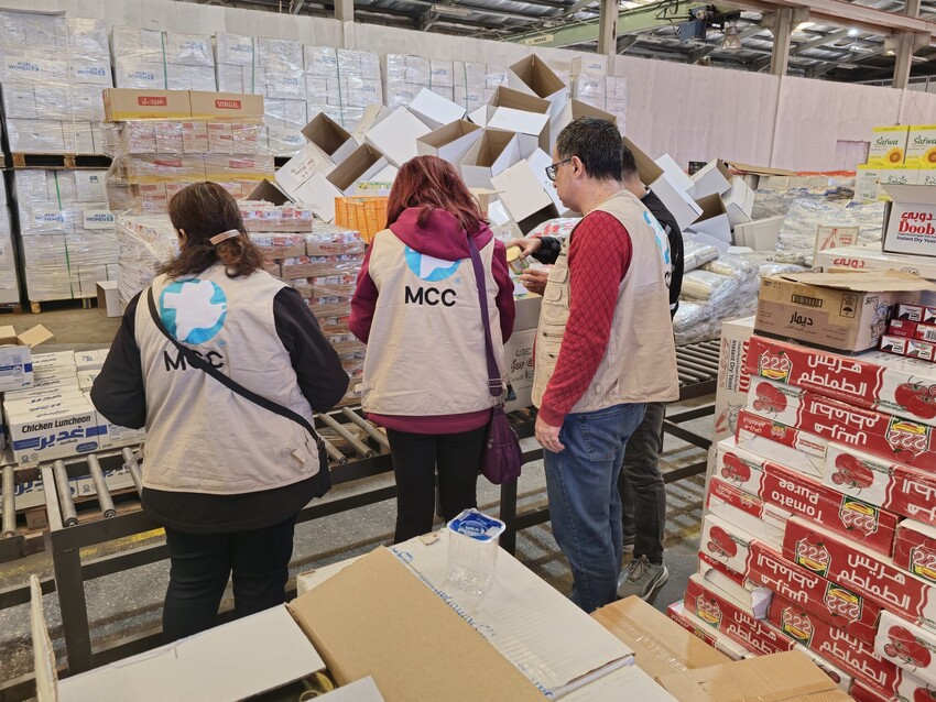 A group of people in MCC vests observe food packing in a warehouse