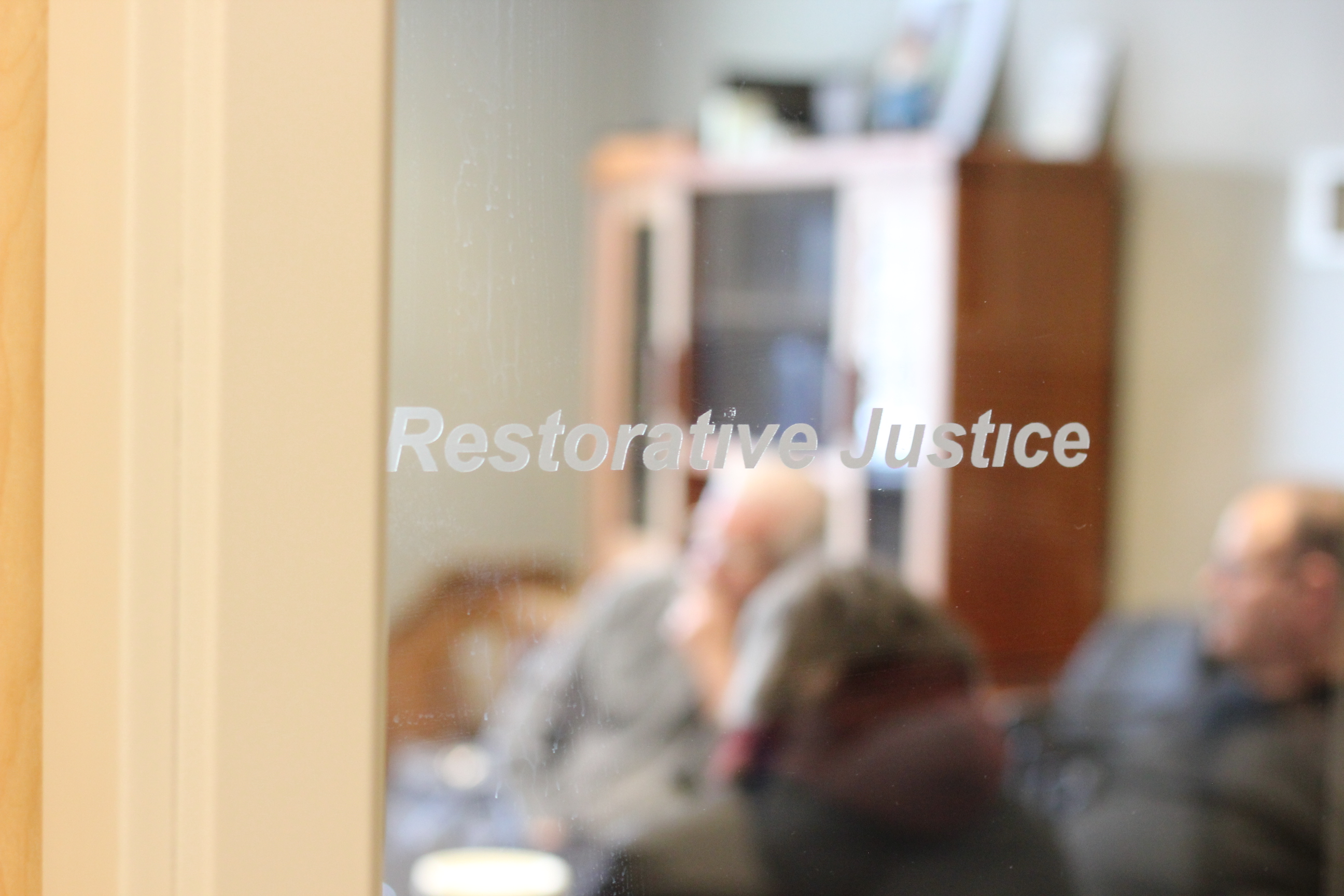 group of people in a meeting viewed through frosted glass with the words Restorative Justice on the glass